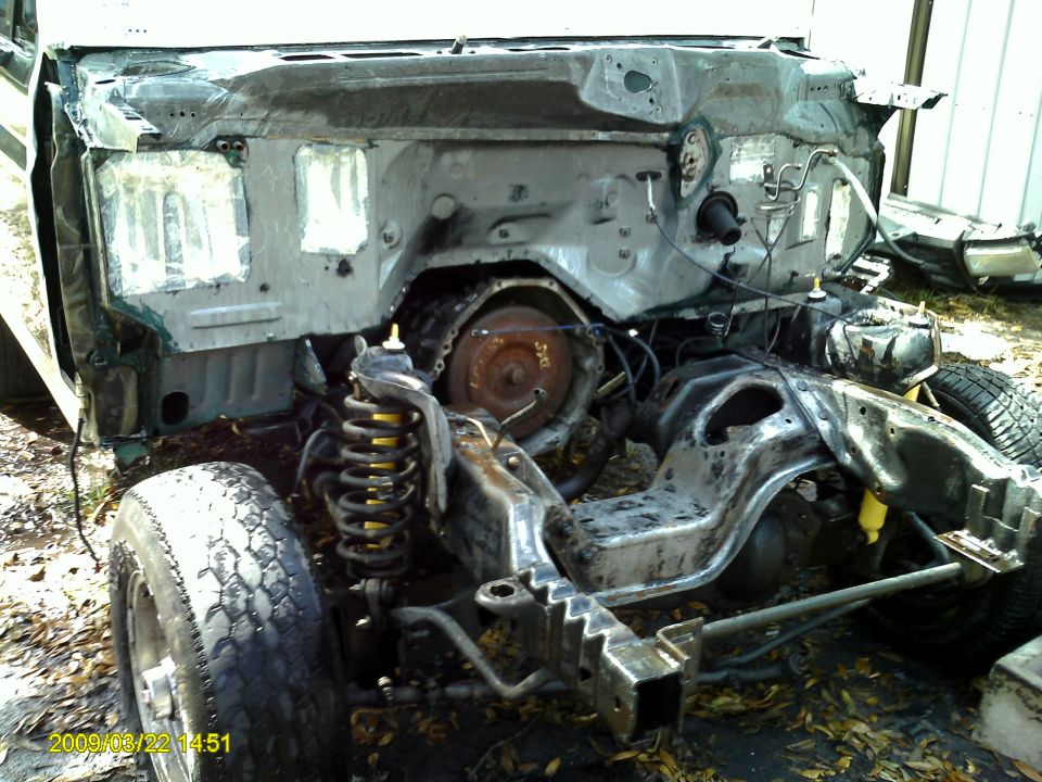 Disassembled vehicle chassis with exposed engine and suspension components, front view