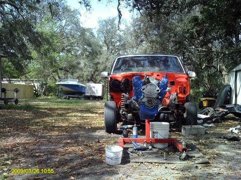 1992 Ford Bronco - An orange SUV is undergoing engine work in a yard, with a boat visible in the background.