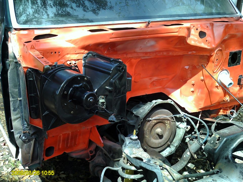 Disassembled vehicle engine bay with orange firewall, black blower motor, and transmission torque converter visible