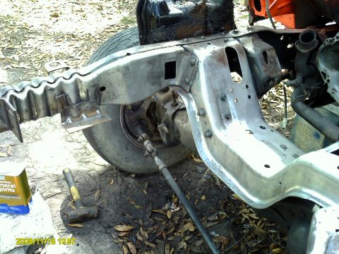 1992 Ford Bronco - A close-up view of a vehicle's frame and suspension system, with tools and a can of mineral spirits on the ground.