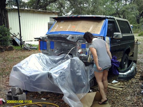 1992 Ford Bronco - A 1992 Ford Bronco's front end is disassembled and covered in plastic sheeting as a person works on it.