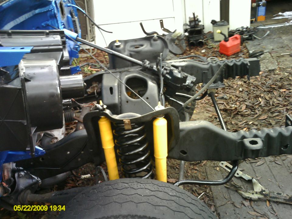 Front suspension and chassis of a vehicle, possibly a truck or SUV, with yellow shock absorbers and black springs. Some blue body panels are visible