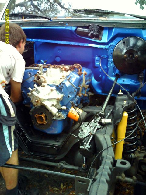 1992 Ford Bronco - A person works on a blue engine installed in a vehicle's engine bay, with an orange oil filter prominent.