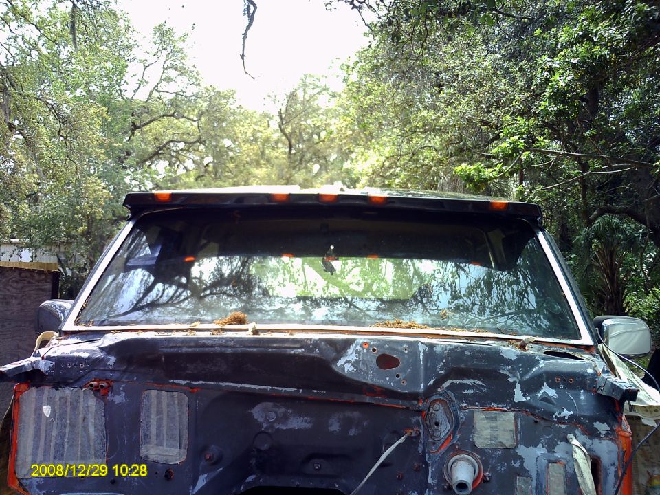 Demolished 1980s Ford Bronco front end, showing rusted chassis and missing grille