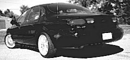 1999 Ford Taurus - This black sedan, likely a 1999 Ford Taurus, is shown from the rear with custom wheels and a spoiler.
