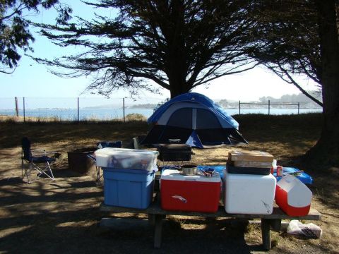 1989 Ford Bronco - A campsite scene unfolds with a blue tent, various coolers, and a picnic table set up near the water.