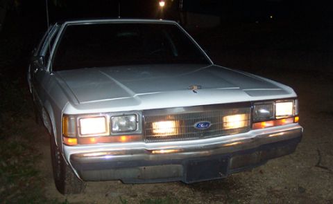 1991 Ford Crown Victoria LTD - A white Ford Crown Victoria is parked outside at night, its headlights illuminating the grille and front end.