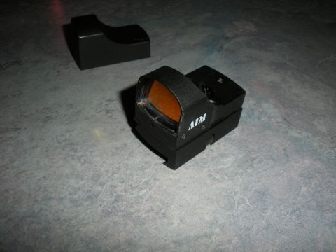 1996 Ford Bronco - A close-up view of an AIM red dot sight and its accompanying mount, resting on a gray, textured surface.