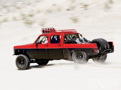 1986 Ford Bronco - This modified pickup truck, equipped for off-road racing, kicks up dust as it speeds across a sandy terrain.