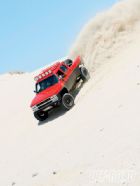 1986 Ford Bronco - A red pickup truck navigates a steep sand dune, creating a large plume of displaced sand.