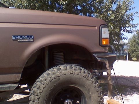 1993 Ford Bronco - Close-up of a brown Ford Bronco's front fender, tire, and suspension system.