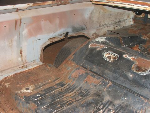1963 Ford Fairlane - The interior of a car's trunk shows extensive rust and damage to the floor and wheel well area.