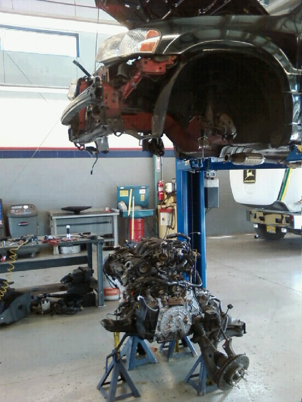 Car body on blue lift with engine and subframe removed onto jack stands in a shop