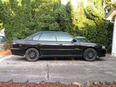 1998 Subaru Legacy - Side view of a black 1998 Subaru Legacy sedan, gunmetal wheels and a subtle rear spoiler.