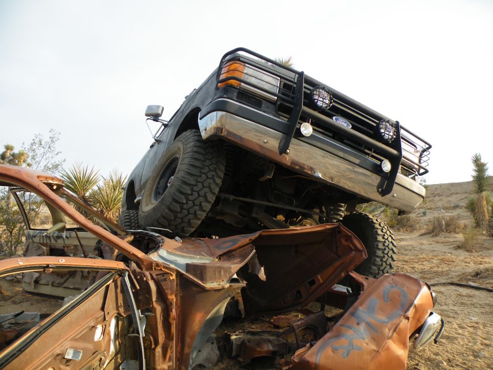 1990 Ford Bronco on top of a wrecked car in a junkyard