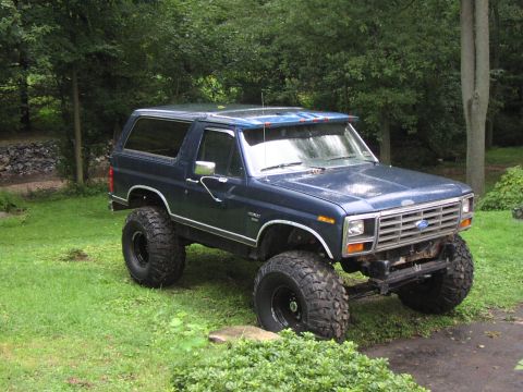 1986 Ford Bronco - A lifted 1986 Ford Bronco sits on a grassy lawn with trees in the background.