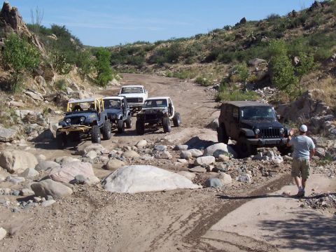 1981 Ford F-150 - A group of off-road vehicles, including Jeeps and a pickup truck, traverse a challenging, rocky terrain on a sunny day.