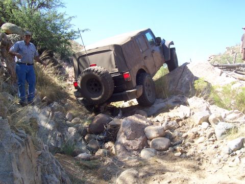 1981 Ford F-150 - A man watches a Jeep Wrangler navigate a steep, rocky incline off-road.