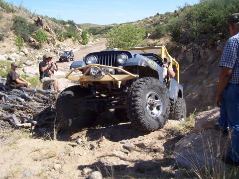 1981 Ford F-150 - A heavily modified Jeep CJ-7 navigates a challenging off-road trail with spectators watching.