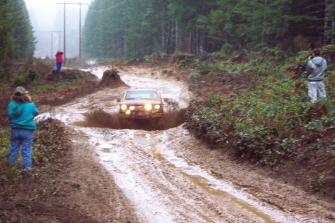 1989 Ford F-150 - A 1989 Ford F-150 navigates a muddy track in a forest setting, with onlookers observing the off-road action.