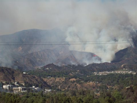 1990 Ford Bronco - An air tanker drops retardant on a hillside fire, with smoke obscuring the mountain peaks and a town below.