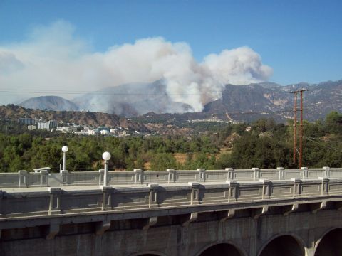 1990 Ford Bronco - Wildfire smoke rises over mountains near a town, seen from a bridge.