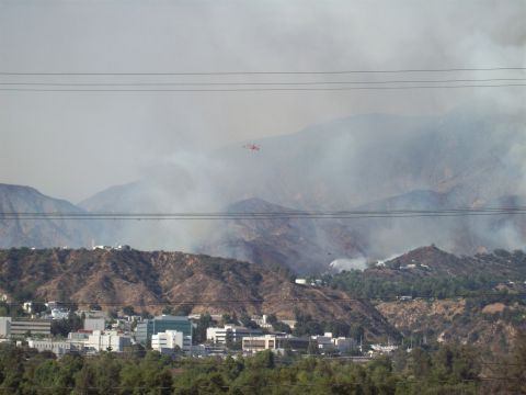 1990 Ford Bronco - A helicopter flies through smoke billowing from a wildfire in the mountains above a suburban area.