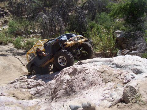 1981 Ford F-150 - A heavily modified Jeep navigates a rocky, off-road trail with a driver visible.