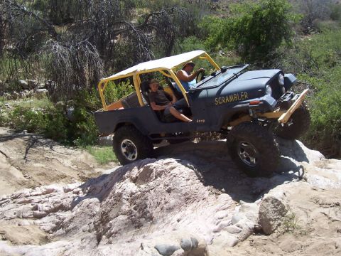 1981 Ford F-150 - A dark blue Jeep CJ-8 Scrambler navigates a rocky trail with two occupants inside.