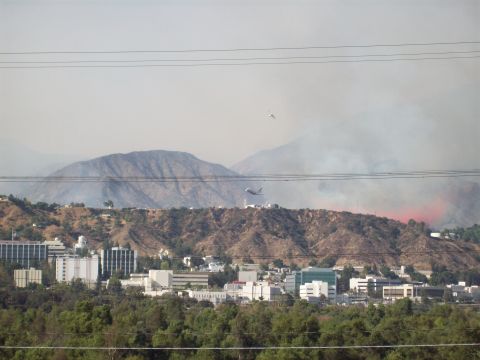 1990 Ford Bronco - An air tanker drops water on a hillside wildfire, with buildings and trees visible below.