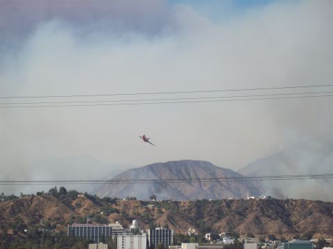 1990 Ford Bronco - An air tanker flies over a smoky landscape with buildings and hills visible.