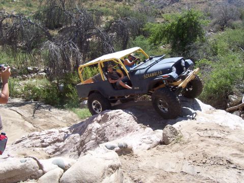 1981 Ford F-150 - A Jeep CJ-8 Scrambler navigates a rocky off-road trail with two occupants.