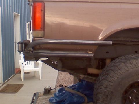 1993 Ford Bronco - Side view of a shop-fabricated bare-steel rear bumper being fitted to a tan Ford truck, made from square tube with a rounded tubular upper…