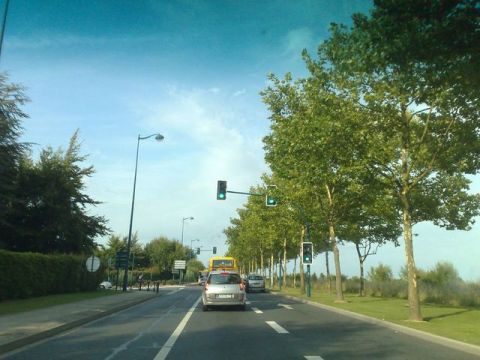 1991 Ford LTD Crown Victoria - A silver car travels down a road lined with trees and traffic lights under a blue sky.