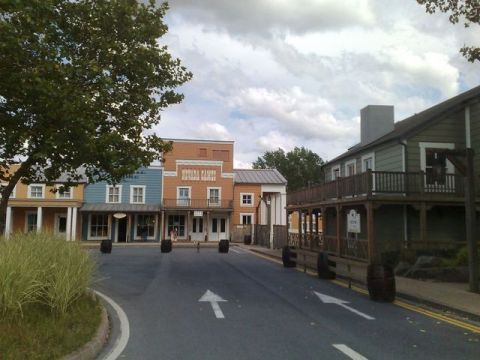 1991 Ford LTD Crown Victoria - A street scene in a western-themed town, buildings with period-appropriate architecture and barrels lining the road.