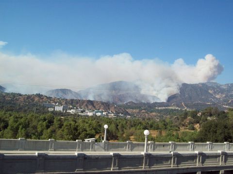 1990 Ford Bronco - Smoke from a wildfire rises into the sky, with buildings visible in the foothills below.