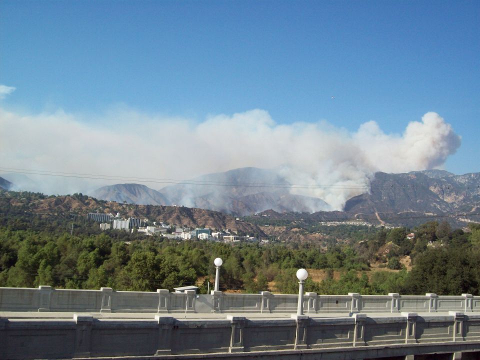Wildfire smoke billows from mountainside near buildings