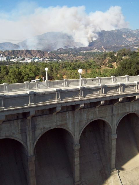 1990 Ford Bronco - Wildfire smoke rises from hills in the distance, seen from a concrete bridge.