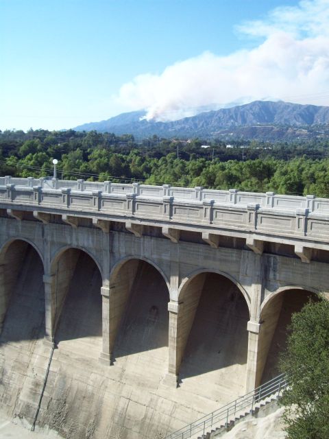 1990 Ford Bronco - Smoke plumes rise from a distant mountain range, seen over a large concrete dam.