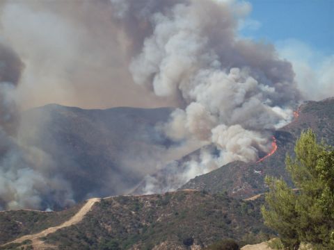 1990 Ford Bronco - A wildfire rages on a dry, mountainous terrain, sending thick smoke into the clear blue sky.