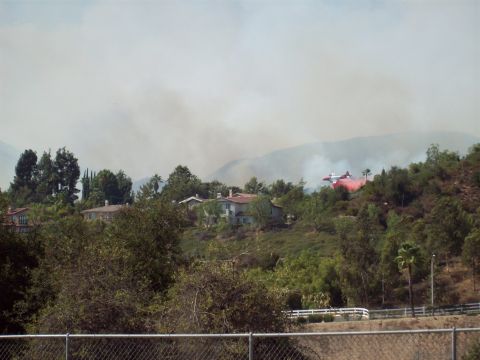 1990 Ford Bronco - An air tanker drops retardant over a hillside fire, with homes visible in the background.