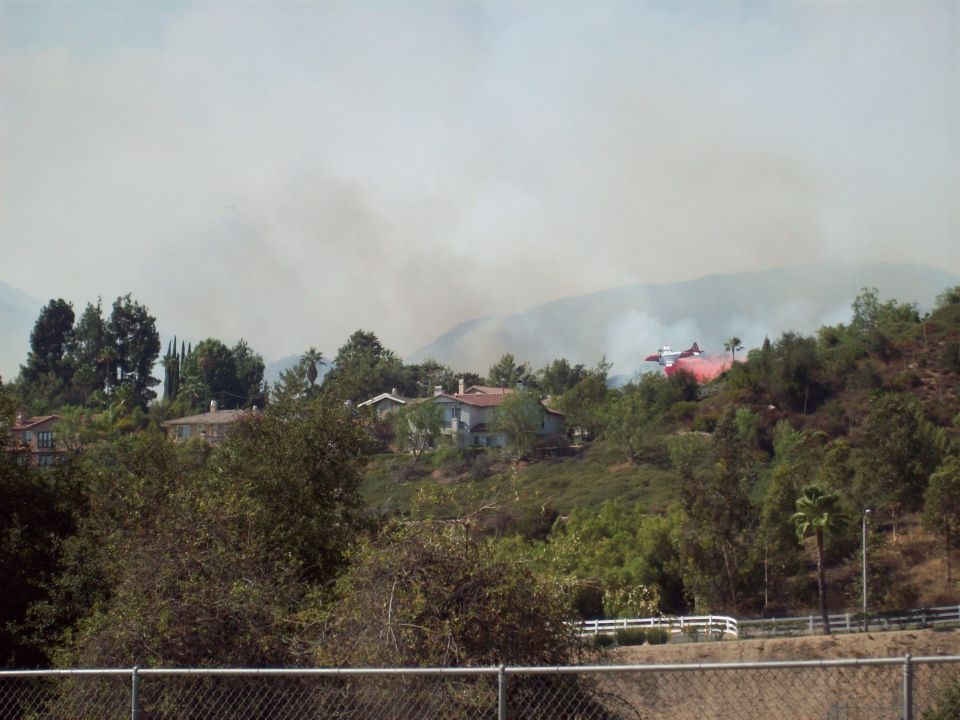 Air tanker dropping red retardant on hillside fire near houses