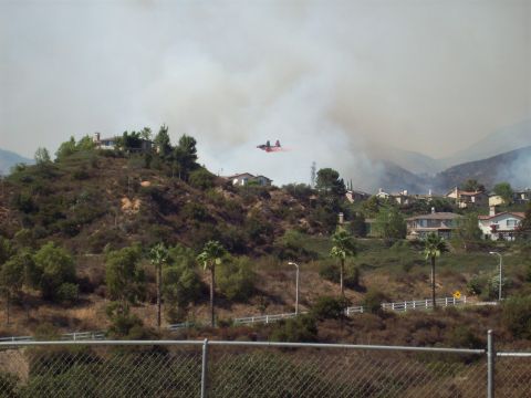 1990 Ford Bronco - A firefighting plane drops retardant amidst smoke and houses on a hillside.