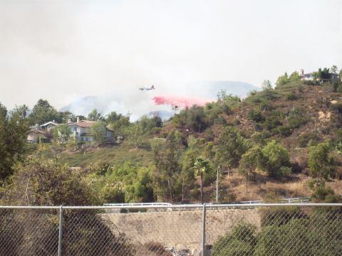 1990 Ford Bronco - An air tanker drops retardant on a hillside fire, with houses visible in the background.