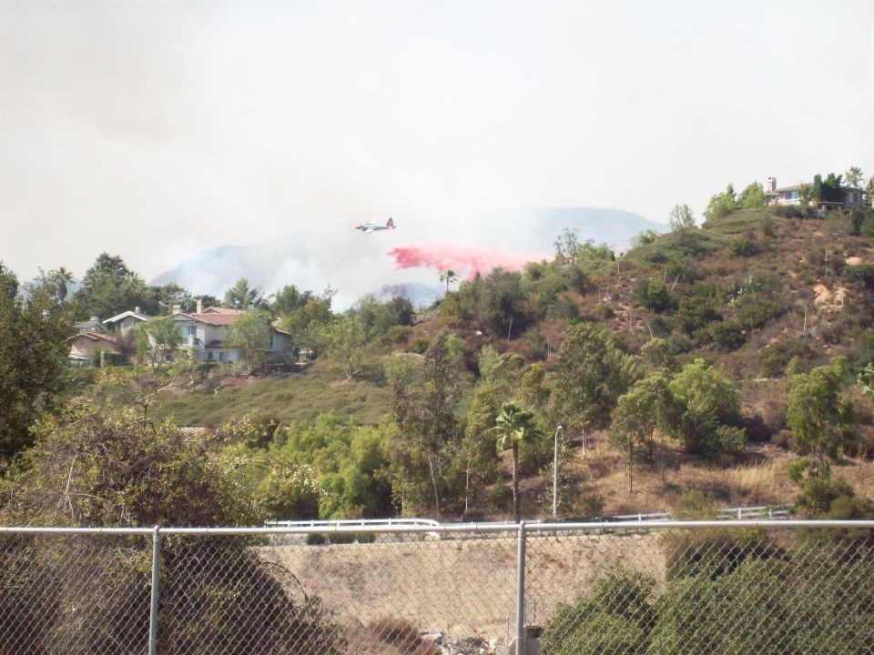 Air tanker drops red retardant over a hillside with houses and trees