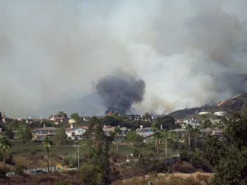1990 Ford Bronco - A large wildfire spreads smoke across the sky over a residential area with homes in the hills.