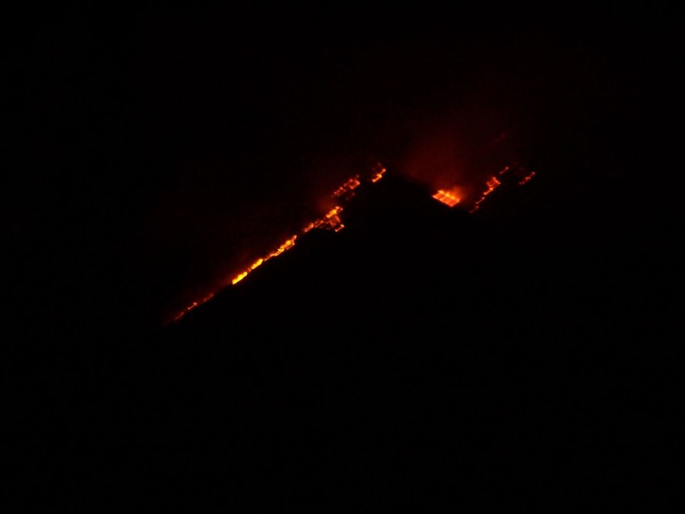 Hillside burning with orange flames against a black night sky