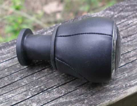2010 Hyundai Genesis - A black leather shift knob with chrome trim rests on a weathered wooden surface.