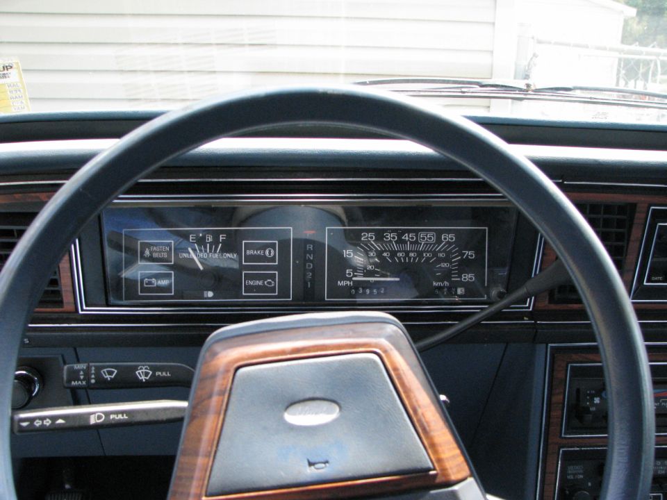 Dashboard view of a 1985 Ford LTD, showing the steering wheel, instrument cluster with speedometer and fuel gauge, and wood-grain trim