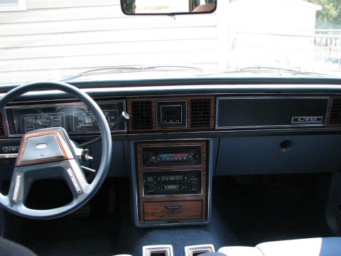 1985 Ford LTD - The interior of a 1985 Ford LTD shows a dashboard with wood grain accents and a prominent steering wheel.